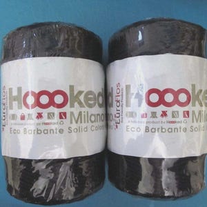 May include: Two dark brown spools of yarn, wrapped in clear plastic. Each spool has a white label with the text "Hoooked Milano Eco Barbante Solid Color". The background is a light blue.