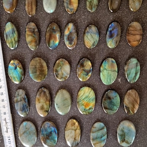 May include: Twenty-five oval-shaped labradorite stones, each with a unique iridescent sheen, ranging from dark gray to blue and green.