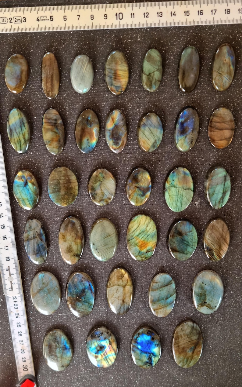 May include: Twenty-five oval-shaped labradorite stones, each with a unique iridescent sheen, ranging from dark gray to blue and green.