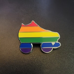 May include: A colorful roller skate pin with a rainbow design. The pin features a vibrant spectrum of colors, including red, orange, yellow, green, blue, and purple, with a silver outline. The wheels are purple and blue.