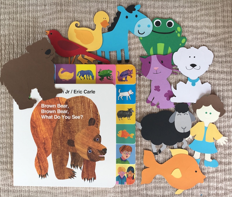May include: A children's book titled "Brown Bear, Brown Bear, What Do You See?" by Bill Martin Jr. and Eric Carle. The book cover features a brown bear with a yellow background. The book is surrounded by colorful paper cutouts of animals, including a blue horse, a green frog, a purple cat, a white dog, a black sheep, a yellow fish, and a girl with brown hair wearing a yellow shirt and blue skirt.