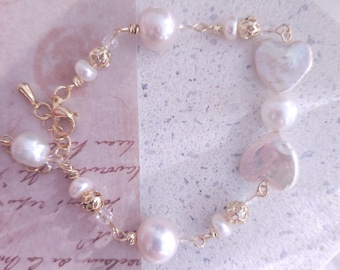Peut inclure: Un bracelet délicat en chaîne dorée avec des perles blanches et des breloques en forme de cœur. Le bracelet est doté d'un fermoir à homard.