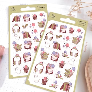 Op de afbeelding: Twee stickervellen met een lichtgroene rand met een herhalend patroon van illustraties met paddenstoelen. De stickers bevatten paddenstoelen, boeken, koptelefoons en potplanten. De tekst "Mushroom Studying Vinyl Sticker" staat rechtsboven.