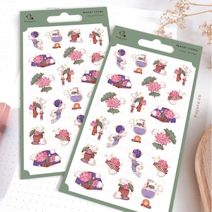 Op de afbeelding: Twee sticker vellen met waterlelie ontwerpen. De stickers tonen roze lotusbloemen, paarse waaiers, zwaarden en drankflessen. De tekst "Water Lilies Vinyl Sticker" staat bovenaan de vellen.
