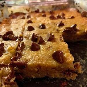 Puede incluir: Primer plano de una bandeja de barras de galletas reci&eacute;n horneadas. Las barras son de color marr&oacute;n dorado con chispas de chocolate. Las barras est&aacute;n cortadas en cuadrados, listas para servir. Un dulce casero.