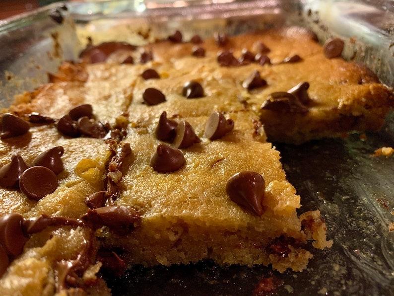 Puede incluir: Primer plano de una bandeja de barras de galletas reci&eacute;n horneadas. Las barras son de color marr&oacute;n dorado con chispas de chocolate. Las barras est&aacute;n cortadas en cuadrados, listas para servir. Un dulce casero.