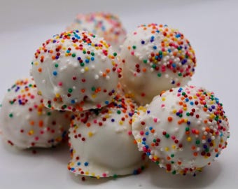 May include: A pile of white cake pops covered in a white chocolate coating and colorful sprinkles. The cake pops are round and stacked on top of each other, creating a visually appealing dessert.