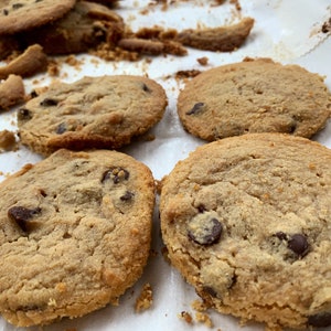 K&ouml;nnte beinhalten: Nahaufnahme von mehreren frisch gebackenen Schokoladen-Chip-Cookies auf einem Backblech. Die Kekse sind goldbraun mit sichtbaren Schokoladenst&uuml;ckchen. Einige Kekse sind ganz, andere haben zerbrochene St&uuml;cke.