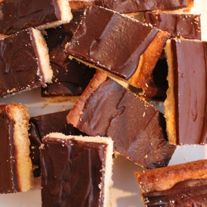 May include: A close-up shot of several rectangular chocolate-covered shortbread cookies. The cookies have a light-colored, crumbly base topped with a layer of dark chocolate. Some cookies are cut, revealing the layers. The image is well-lit, highlighting the textures.
