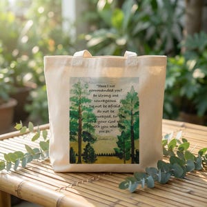 Puede incluir: Un bolso tote de lona beige con una impresión de acuarela de árboles y texto. El texto dice: "¿No te he mandado? Sé fuerte y valiente. No temas..." Josué 1:9 también está impreso en la bolsa.