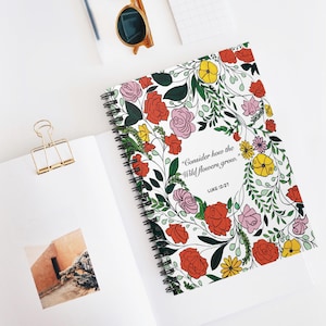 May include: A floral notebook with a spiral binding. The cover displays a wreath of red, pink, and yellow flowers with green leaves. The text on the cover reads, "Consider how the wild flowers grow." and "Luke 12:27."