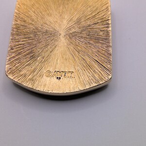 May include: Gold-toned pendant with a textured surface and the word "GAYLA" engraved on the back.