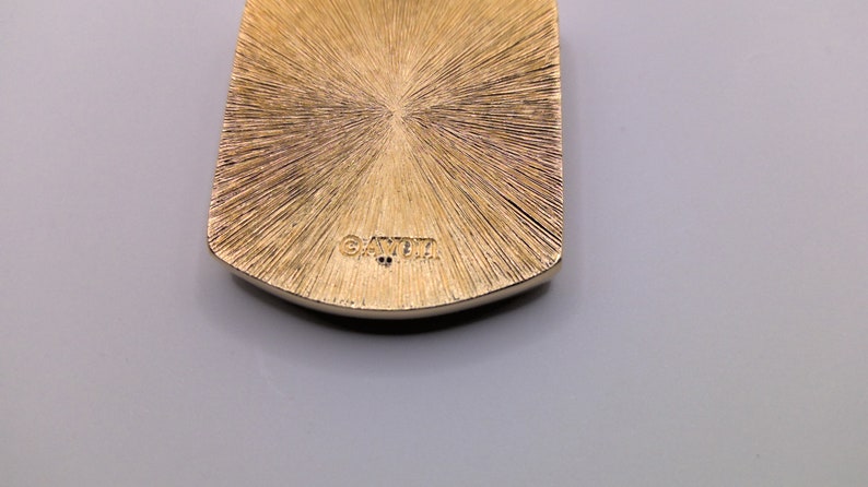 May include: Gold-toned pendant with a textured surface and the word "GAYLA" engraved on the back.
