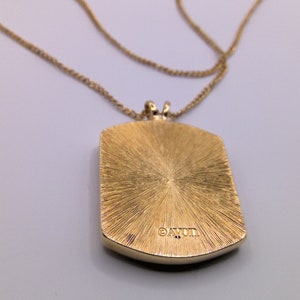 May include: Gold tone necklace with a square pendant that has a textured surface and the word "AVON" engraved on the back.