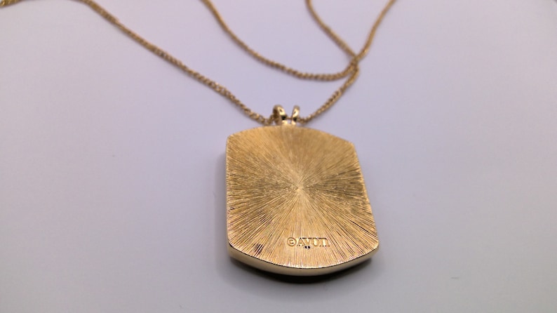 May include: Gold tone necklace with a square pendant that has a textured surface and the word "AVON" engraved on the back.