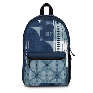 Könnte beinhalten: Ein marineblauer Rucksack mit einer Vordertasche und einem schwarzen Reißverschluss. Der Rucksack hat ein geometrisches Muster in Blau- und Weißtönen. Das Design umfasst Quadrate, Kreise und vertikale Linien.