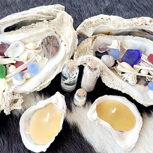 May include: Two oyster shells filled with sea glass, shells, and other beach treasures.  Two small glass bottles with cork tops contain sand and sea life.  Two oyster shells are filled with yellow candles.