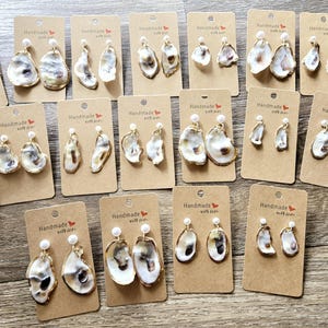 May include: Assortment of oyster shell earrings with pearl accents on brown card stock with the text "Handmade with Love" printed on each card.