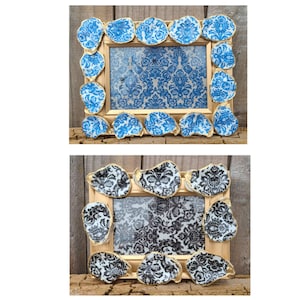 May include: Two gold picture frames decorated with blue and black oyster shells. The frames are both rectangular and have a white background with a damask pattern.