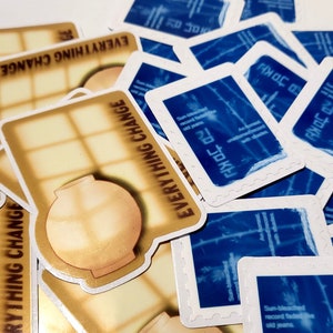 May include: A stack of stickers with a blue and white design featuring the text "PHOTOC" and "EVERYTHING CHANGE". The stickers are on a white surface.