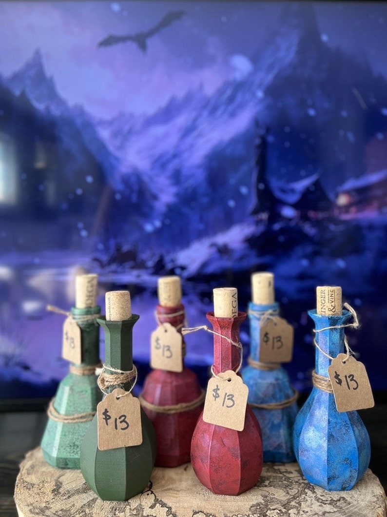 May include: Six small glass bottles with cork stoppers and brown paper tags with the price $13 written on them. The bottles are filled with different colored liquids and have a textured, faceted design. The bottles are arranged in a row on a wooden surface.