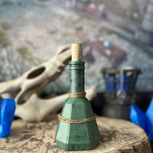 May include: A green glass bottle with a cork stopper and a twine wrap. The bottle is sitting on a wooden surface.