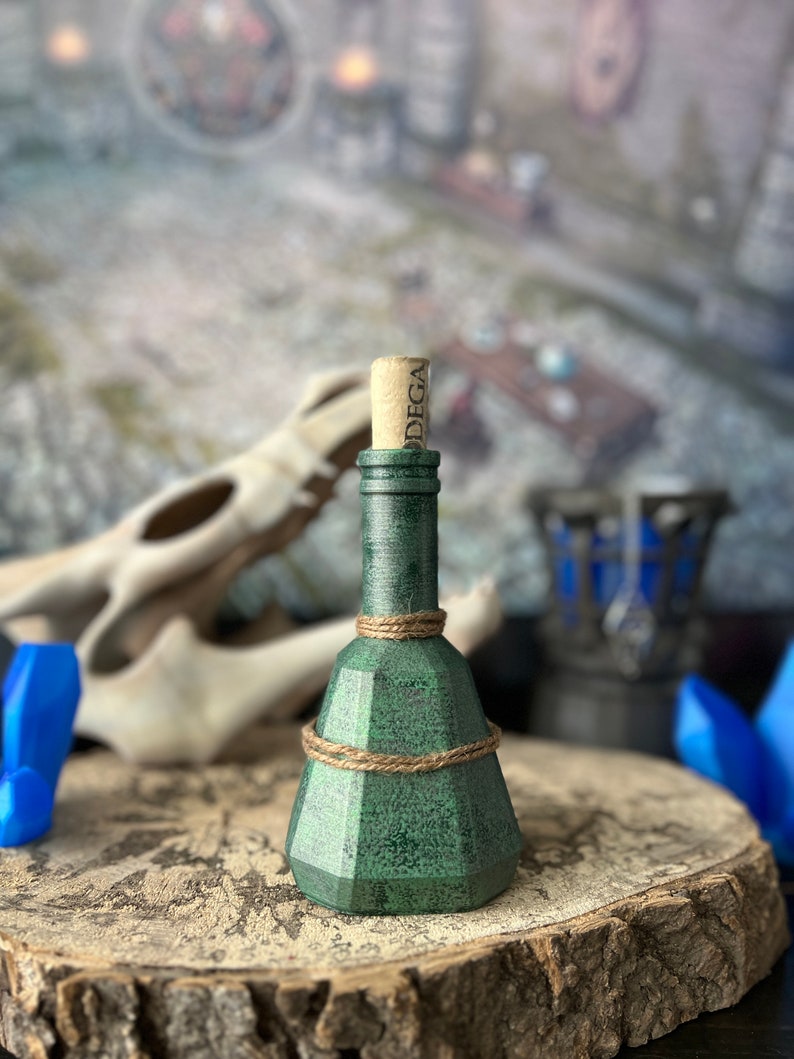 May include: A green glass bottle with a cork stopper and a twine wrap. The bottle is sitting on a wooden surface.