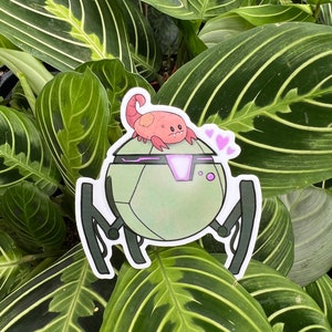 Op de afbeelding: Een groene en paarse robot met een kleine, roze, cartoonachtige schorpioen erop. De robot heeft drie poten en een rond lichaam. De schorpioen heeft een klein, roze hart boven zijn kop.