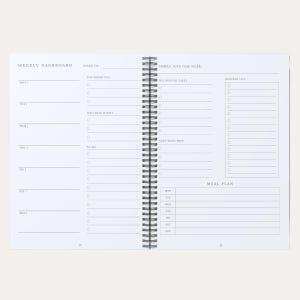 May include: A white spiral-bound weekly planner open to two pages. The left page features a Weekly Dashboard with daily sections. The right page includes sections for Simple Joys, Household Tasks, Grocery List, Next Week Prep, and a Meal Plan.