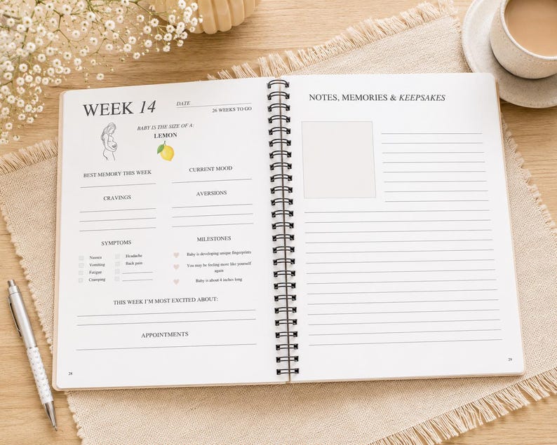 May include: A spiral-bound pregnancy journal open to week 14. The left page features sections for date, baby size as a lemon, mood, cravings, aversions, symptoms, milestones, and appointments. The right page has lined space for notes, memories, and keepsakes.