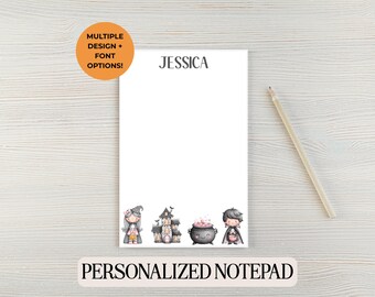 Może przedstawiać: Biały spersonalizowany notatnik z imieniem "JESSICA" na górze. Na dole notatnika znajduje się ilustracja o tematyce Halloween z czarownicą, nawiedzonym domem, kotłem i młodym czarodziejem. Ołówek leży z boku. Tekst brzmi "PERSONALIZED NOTEPAD".