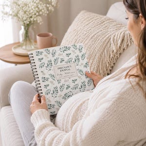 May include: A spiral-bound pregnancy journal with a white cover featuring a green botanical leaf pattern. The center label displays the text PREGNANCY JOURNAL, Baby Williams, and DUE JANUARY 2027 in black ink. The journal has a black wire binding.