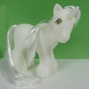 May include: A white unicorn pony toy with a long white mane and tail. The pony has yellow eyes and a pink nose.