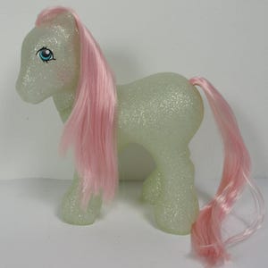 May include: A light green glittery My Little Pony with pink hair. The pony has blue eyes and a pink nose.