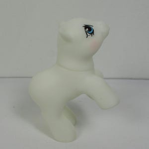 May include: A white glow-in-the-dark pony toy with blue eyes and a pink blush. The pony is standing on its hind legs with its front legs raised.