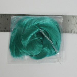 Könnte beinhalten: Eine türkisfarbene Perücke für eine Puppe, verpackt in einer durchsichtigen Plastiktüte.