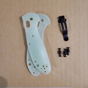 May include: A collection of knife handle scales, a black pocket clip, and small black screws. The handle scales are a pale green color and have several holes. The pocket clip is made of black metal.