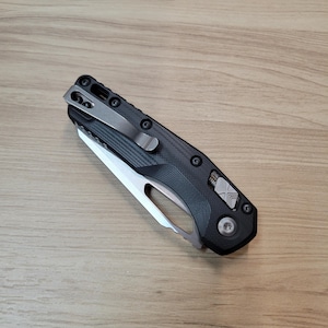 May include: A black folding knife with a silver blade and a textured black handle. The knife has a pocket clip and a safety lock.