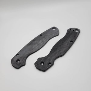 May include: Two black carbon fiber knife scales with rounded edges and multiple holes.