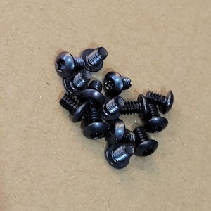 May include: A pile of black screws with a star-shaped head. The screws are small and have a flat head.