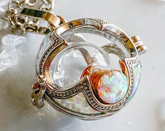 May include: A silver and gold necklace with a clear glass orb pendant. The orb is filled with a white opal stone and has a delicate silver chain.