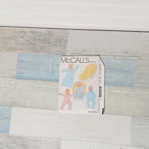 May include: A McCall's pattern book featuring illustrations of baby clothing and accessories. The cover displays images of a baby in a blue gown, a yellow car seat, and a pink onesie. The pattern number is 6888.