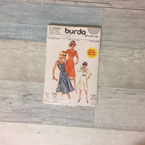 May include: A vintage Burda sewing pattern packet featuring illustrations of three different dresses. The packet is labeled with the number 20982 and includes size information. The cover art depicts women in dresses, with a yellow and red sticker.