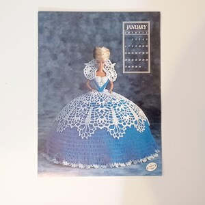 May include: A vintage calendar page featuring a Barbie doll in a crocheted gown. The doll's dress is a combination of blue and white crochet, with a large skirt. The calendar shows the month of January.