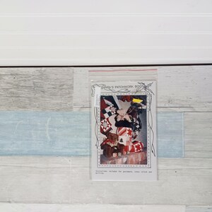 May include: A clear plastic bag containing a printed paper with the text "SANTA'S PATCHWORK BOOT". The image on the paper shows a patchwork boot with a teddy bear and other Christmas-themed elements. Instructions for patchwork, cross stitch, and quilting are included.