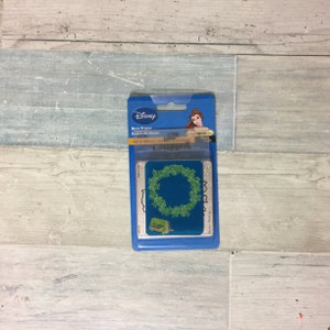 May include: A Disney Rose Frame craft die set in a blue package. The set includes a die with a green rose wreath design and a small green die-cutting machine. The package features Disney branding and an image of Belle.