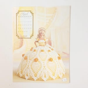 May include: A vintage 1992 calendar page featuring a Barbie doll in a yellow and white crocheted dress. The doll has blonde hair and is posed in front of a soft yellow background. The calendar displays the month of April.
