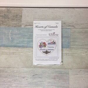 May include: A cross-stitch kit titled "Hearts of Canada" featuring a heart-shaped design with floral and architectural elements. The design includes the word "Victoria" and the Victoria Sampler logo. The kit is sealed in a clear plastic package.