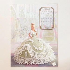 May include: A calendar page featuring a Barbie doll in a green and white crocheted gown. The calendar displays the month of March 1992. The doll has blonde hair and is posed in front of a soft, pastel background.