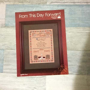 May include: Framed cross-stitch sampler with the text "From This Day Forward." The sampler features a decorative border, alphabet, and the date November 11, 1972. The frame is a dark brown color with a red polka dot border.